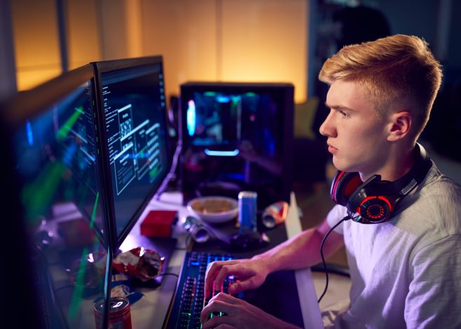 Male Teenage Hacker Sitting In Front Of Computer Screens Bypassing Cyber Security